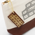 THE SUPERIOR LABOR Engineer Pouch #03 - Chocolate. A long canvas pouch with a hand-painted chocolate bar motif and brass zipper, available in two colors. Pochette Engineer #03 Chocolat par THE SUPERIOR LABOR. Une longue trousse en toile avec un motif de tablette de chocolat peint à la main et zip en laiton.
