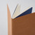 TAKEO PAPER Dressco Stitch Notebook Bister edition. A slim, palm-sized notebook featuring a leather-textured bister brown paper cover, stitched spine, and premium blank Bank Paper pages embedded with a Three Diamonds watermark. / Carnet cousu TAKEO PAPER Dressco Édition Bister. Un carnet de poche mince arborant une couverture en papier brun bister texture cuir, une reliure cousue et des pages blanches en papier de banque haut de gamme.
