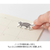 Midori Yuru Log roll sticker in Calligraphy theme, showing a strip of 17 unique elegant script and frame designs being torn from a perforated paper roll. / Rouleau d'autocollants Midori Yuru Log thème Calligraphie, montrant une bande de 17 motifs uniques d'écritures élégantes et de cadres détachée d'un rouleau de papier perforé.