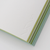 TAKEO PAPER SIKI Notebook M in Wakaba Young Leaves showcasing its unique sloped side profile featuring 49 different green textured paper sheets. / Carnet TAKEO PAPER SIKI Taille M thème Wakaba Jeunes Feuilles montrant son profil en biseau unique composé de 49 feuilles de papiers verts aux textures différentes.