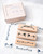 dodolulu Rubber Stamp Set Beholding three-piece beech wood stamp set featuring two girls, a ribbon, and knot motifs. / Ensemble de tampons en caoutchouc dodolulu Beholding comprenant trois tampons en bois de hêtre avec deux filles, un ruban et des motifs de nœuds.
