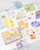 dodolulu 2027 Monthly Calendar Stickers set featuring 12 die-cut calendar cards and 15 decorative stickers with a subtle sand glitter finish in a keepsake box. / Ensemble d'autocollants calendrier mensuel 2027 dodolulu comprenant 12 cartes de calendrier découpées et 15 autocollants décoratifs avec une finition pailletée sablée dans une boîte souvenir.