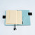 Hobonichi A6 Pocket Envelope. Pack of two self-adhesive paper envelope pockets for A6 with a silver foil logo under the flap and a gusset. Poche-enveloppe Hobonichi A6. Lot de deux pochettes papier autocollantes pour A6, logo argenté sous le rabat et soufflet.