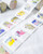 dodolulu 2027 365 Daily Washi Tape Calendar set featuring two rolls of perforated daily washi tape stickers with release paper backing. / Ensemble de rubans washi calendrier 2027 365 jours dodolulu comprenant deux rouleaux d'autocollants perforés quotidiens sur papier protecteur.