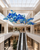 Naola Large Blue Glass Shopping Centre Atrium Chandelier
The Naola chandelier shown spanning a bright modern retail atrium with escalators and upper-level galleries. Its large-scale suspended glass ball composition is ideal for shopping centres, department stores, luxury retail developments and other high-traffic commercial spaces requiring distinctive statement lighting.