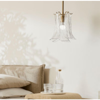 Clear hand-blown glass pendant light with calla lily-inspired shade and antique brass hardware, hanging above a bedside table.