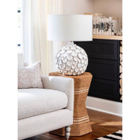 Lucia white ceramic table lamp with pinched disks and a linen shade on a woven side table.