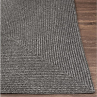 Charcoal gray braided polypropylene outdoor rug with a textured, no-pile surface on a wooden floor.