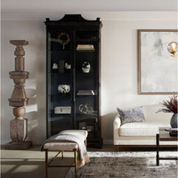 Black iron curio cabinet with glass doors, ornate molding, and five shelves, styled in a living room.