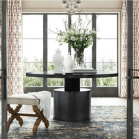 Marlow round black steel dining table with cylindrical base, styled with white vases and flowers.