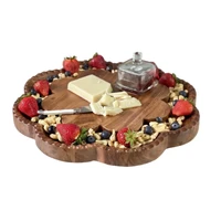 A scalloped wooden charcuterie board filled with peanuts, strawberries, blueberries, and cheese, with a small glass butter dish on a marble surface.