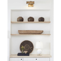 Small natural brass Tate Picture Light illuminating a white wall above shelves with decor.