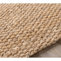 Close-up of a tan, hand-woven jute rug with a textured, no-pile design on a wooden floor.