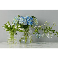 Clear glass wine glass vase with a sphere top, holding small white flowers.