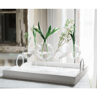 Clear glass wine glass vases with spherical tops, holding white tulips and greenery on a white tray.