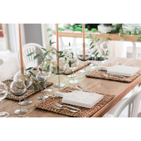Elegant clear small wine glass vases with greenery on a rustic wooden table set for dining.