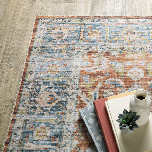 Charleston Rust & Blue Washable Rug with distressed traditional patterns on a wood floor, styled with books and decor.