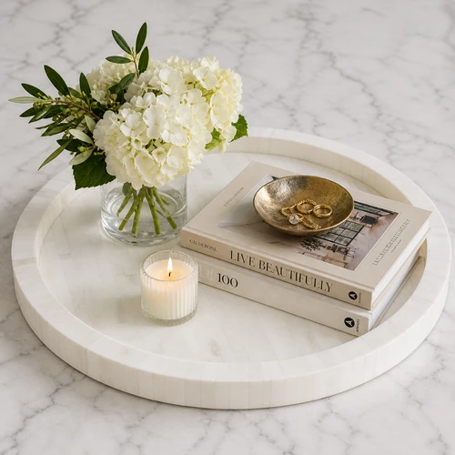 Round Capri natural ivory bone decorative tray holding a vase of hydrangeas, books, a candle, and a gold bowl with jewelry.