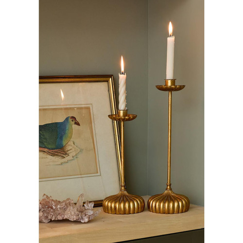 Two antique-style gold Clove candle holders with bobeche detailing and white candles, next to framed bird art.