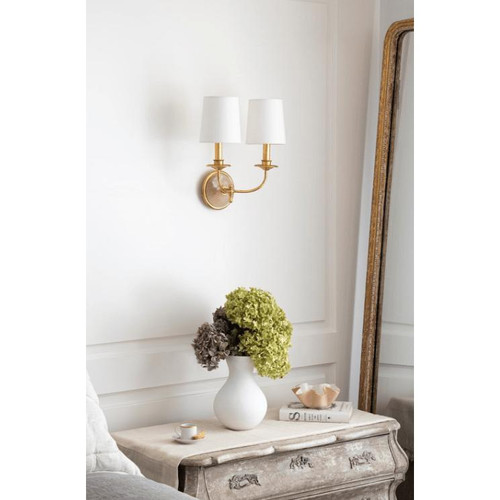 Elegant Fisher Double Sconce with gold leaf finish, alabaster backplate, and two white linen shades mounted on a white wall.