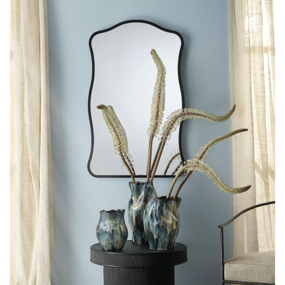 Aurora Wavy Wall Mirror with a thin black metal frame and unique waved edge, hung vertically above three decorative vases.