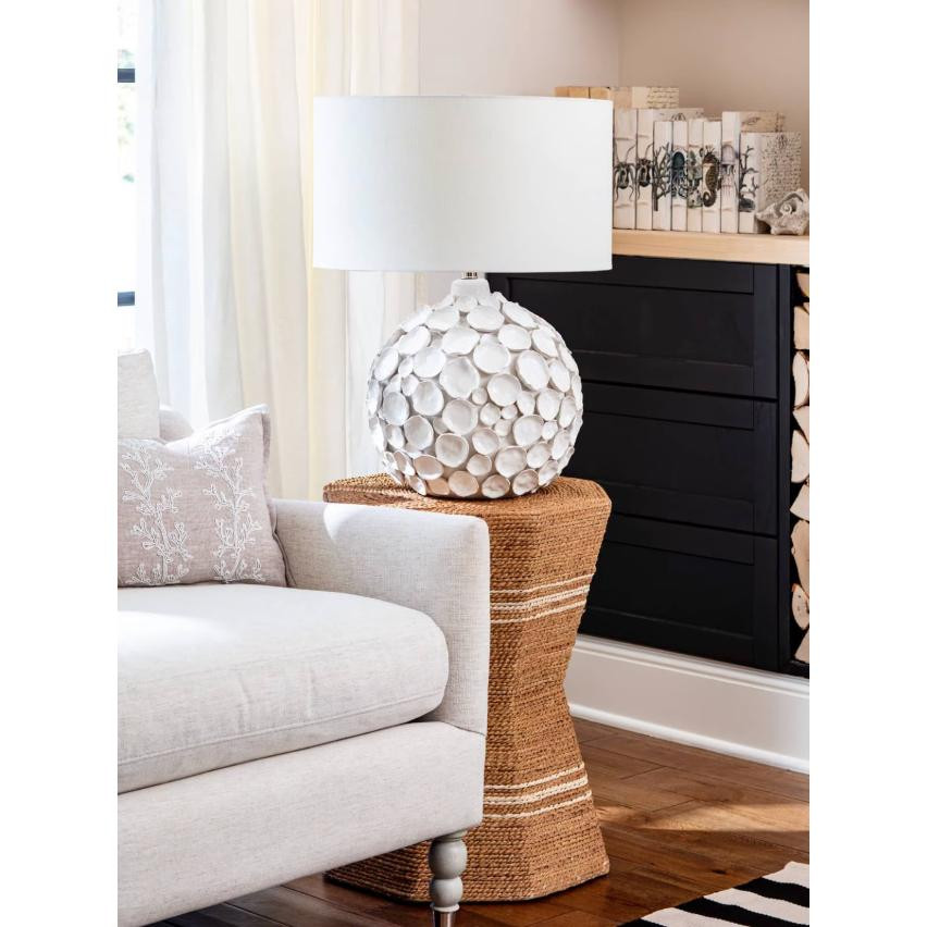Lucia white ceramic table lamp with pinched disks and a linen shade on a woven side table.