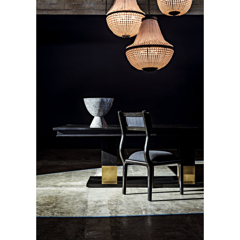 Ravenko black mahogany dining table with brass leg bands, a gray chair, and a decorative bowl under chandeliers.