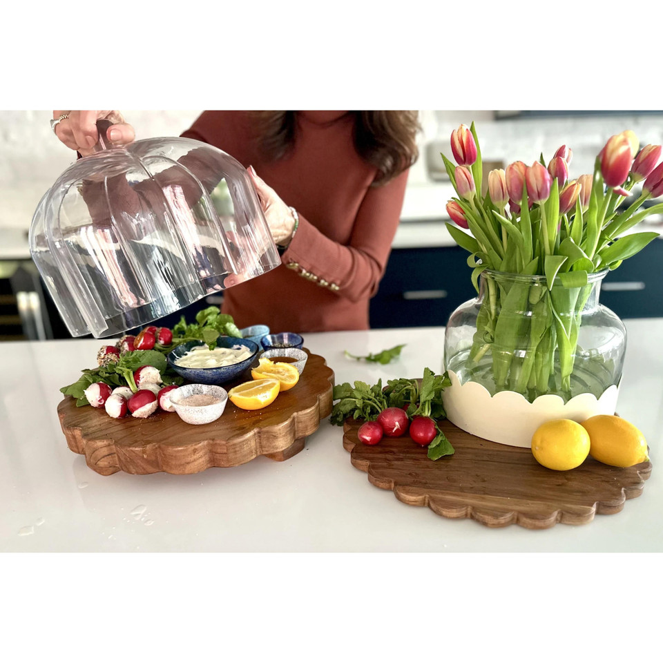 Round scalloped acacia wood charcuterie board with food, next to a matching board and tulips.