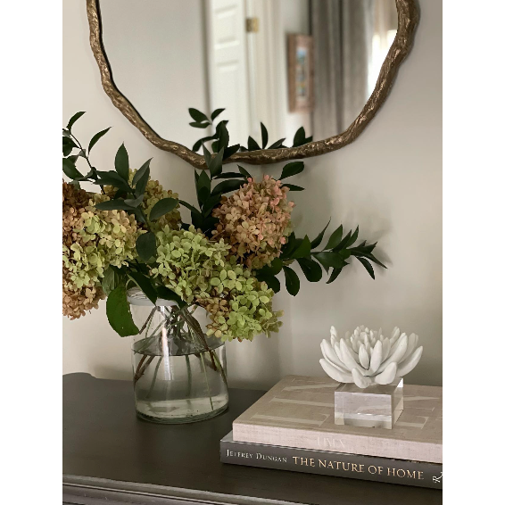 Matte white succulent resin sculpture on a clear acrylic base, next to flowers and books.