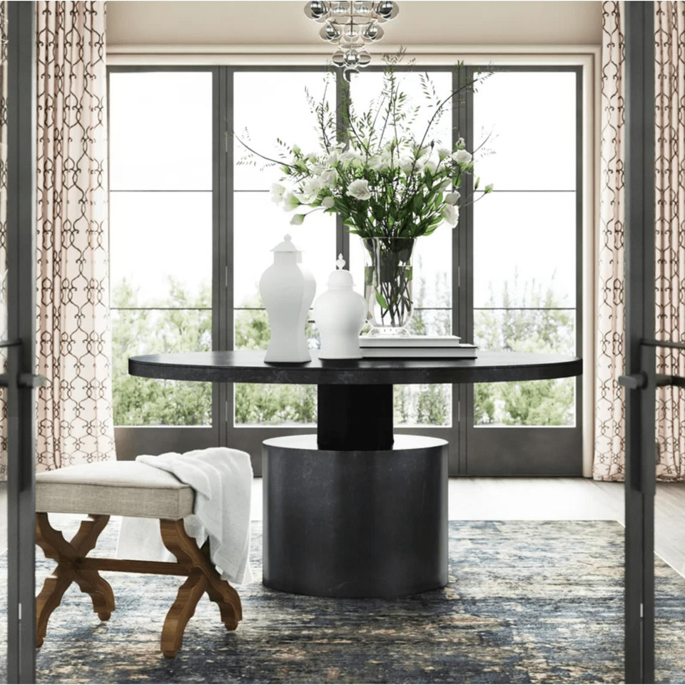 Marlow round black steel dining table with cylindrical base, styled with white vases and flowers.