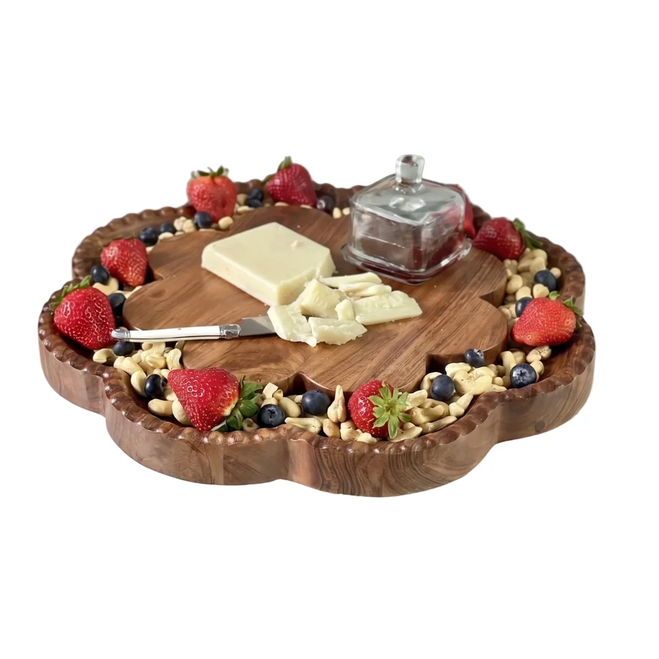 A scalloped wooden charcuterie board filled with peanuts, strawberries, blueberries, and cheese, with a small glass butter dish on a marble surface.