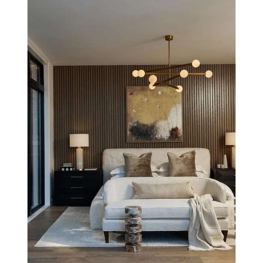 Modern Beaubien Chandelier with eight white globe bulbs and brass arms over a bed.