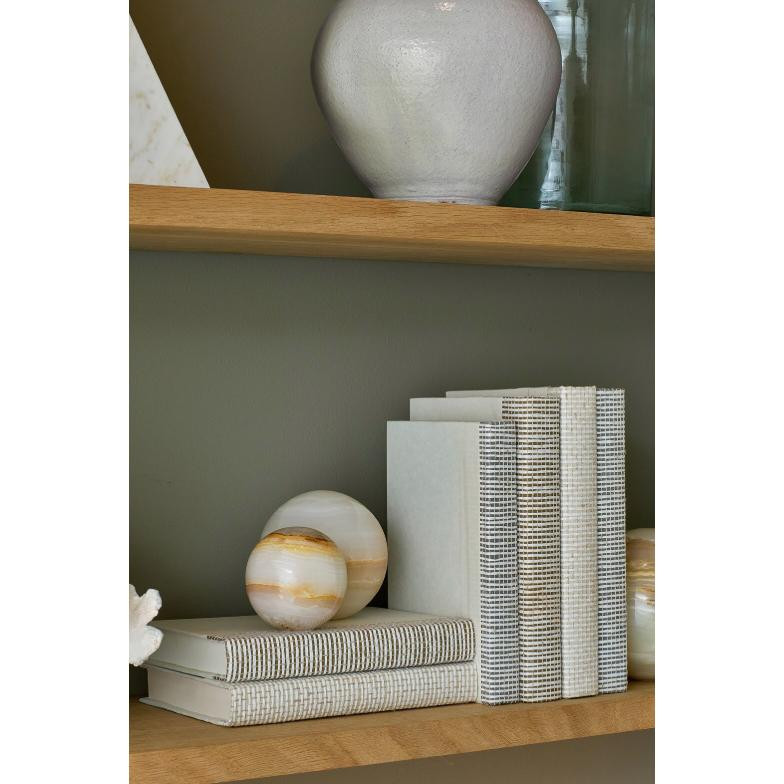 Polished natural jade spheres, one with white and gold marbling, next to white and striped books on a wooden shelf.