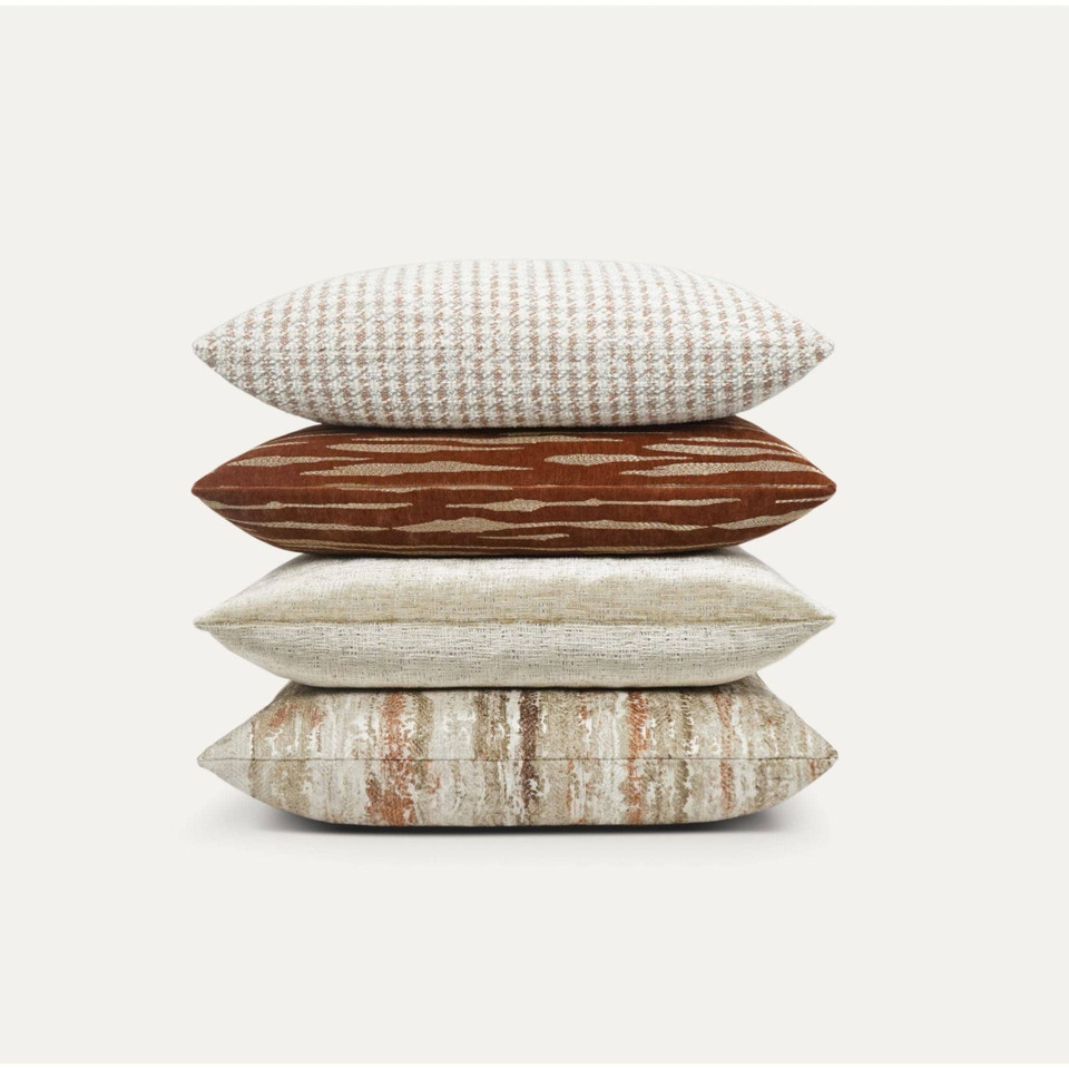Stack of four luxury designer throw pillows in rust, cream, and beige with varied textures.