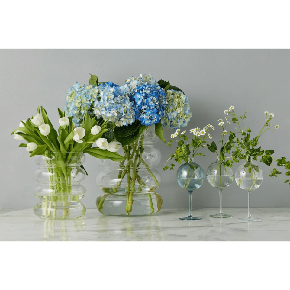 Clear glass wine glass vase with a sphere top, holding small white flowers.