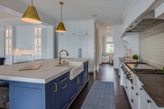 Custom kitchen island with blue shaker panels, quartz countertop, and gold accents paired with white cabinetry
