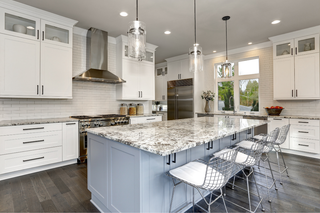Custom kitchen island in a two-tone kitchen with light blue shaker panels and marble countertops