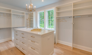 Luxury custom walk-in closet with a center island, cabinetry, drawers, shelving, and hanging storage