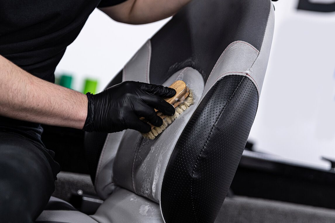 A person cleaning a car's leather seat with a brush.