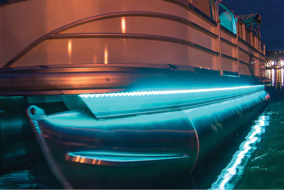 Close-up view of a pontoon boat at night, featuring blue LED strip lighting along the edge of the aluminum pontoon.