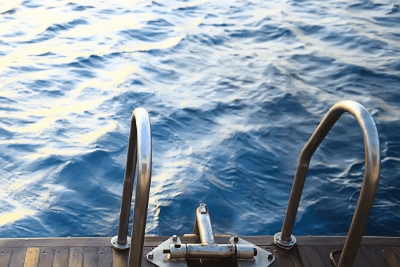Metal swim ladder on boat deck with ocean view.