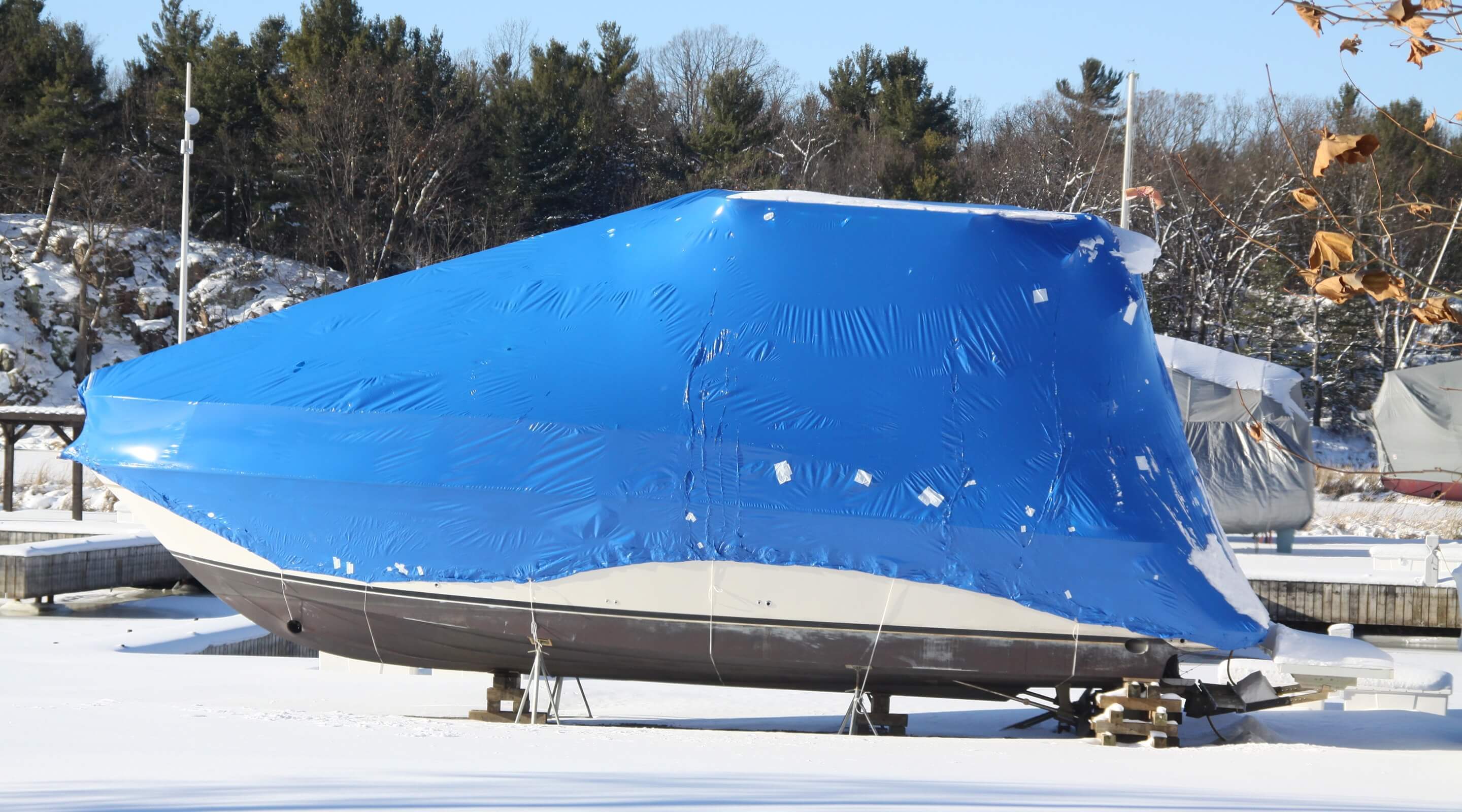 A boat out of the water is protected from the winter elements by a blue cover.
