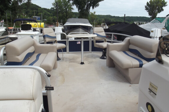 The deck area of a pontoon boat with beige and blue cushioned bench seating on both sides.