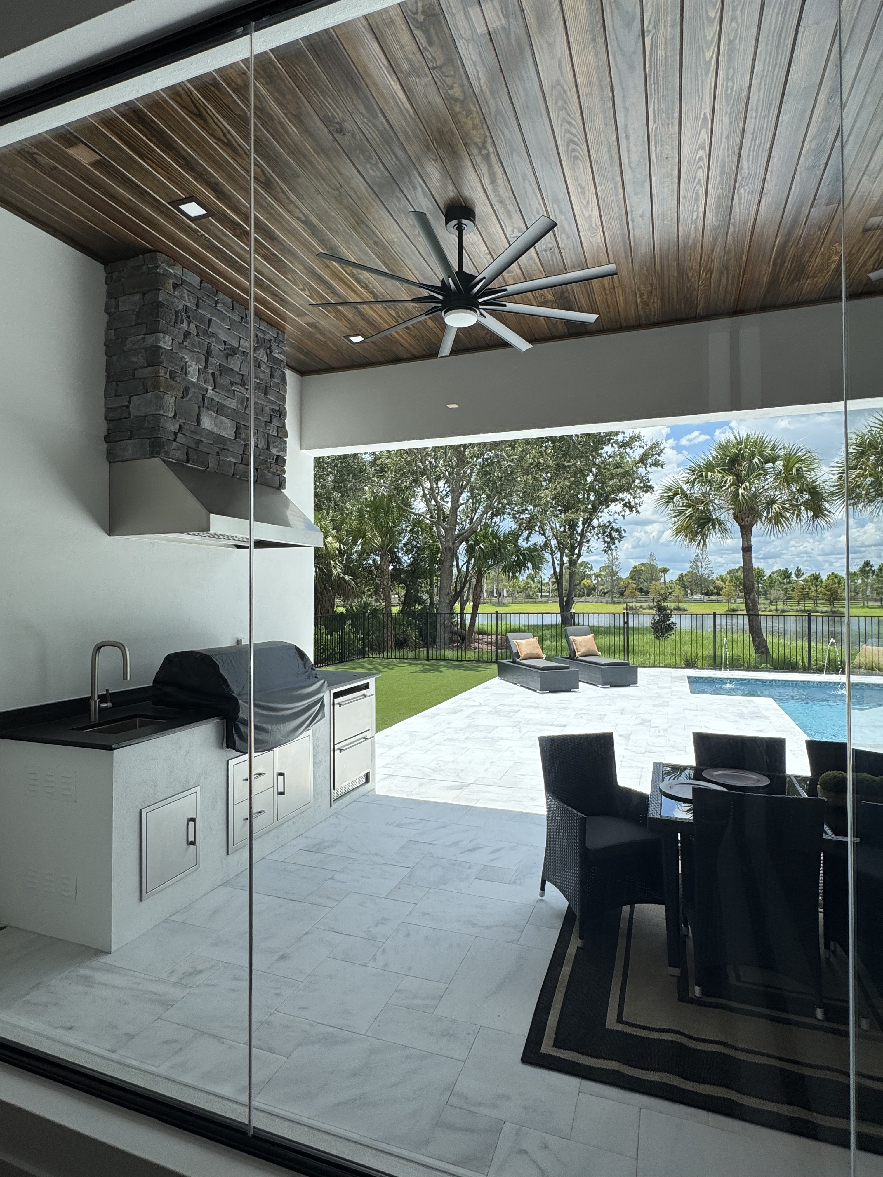 view of back patio through a glass wall with ourdoor kitchen