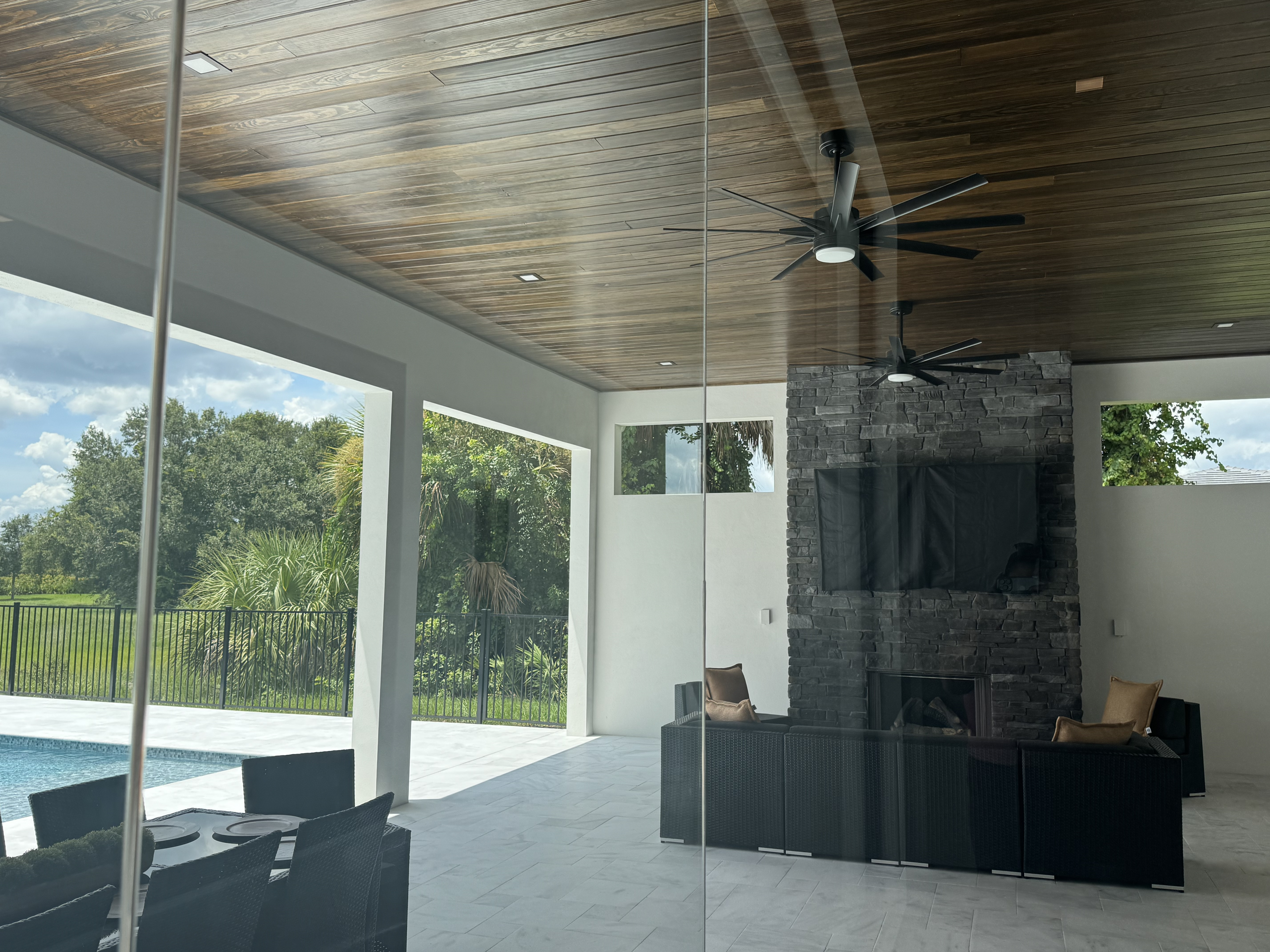 covered patio with shiplap ceiling and glss walls with an firepit with a tv hung above it