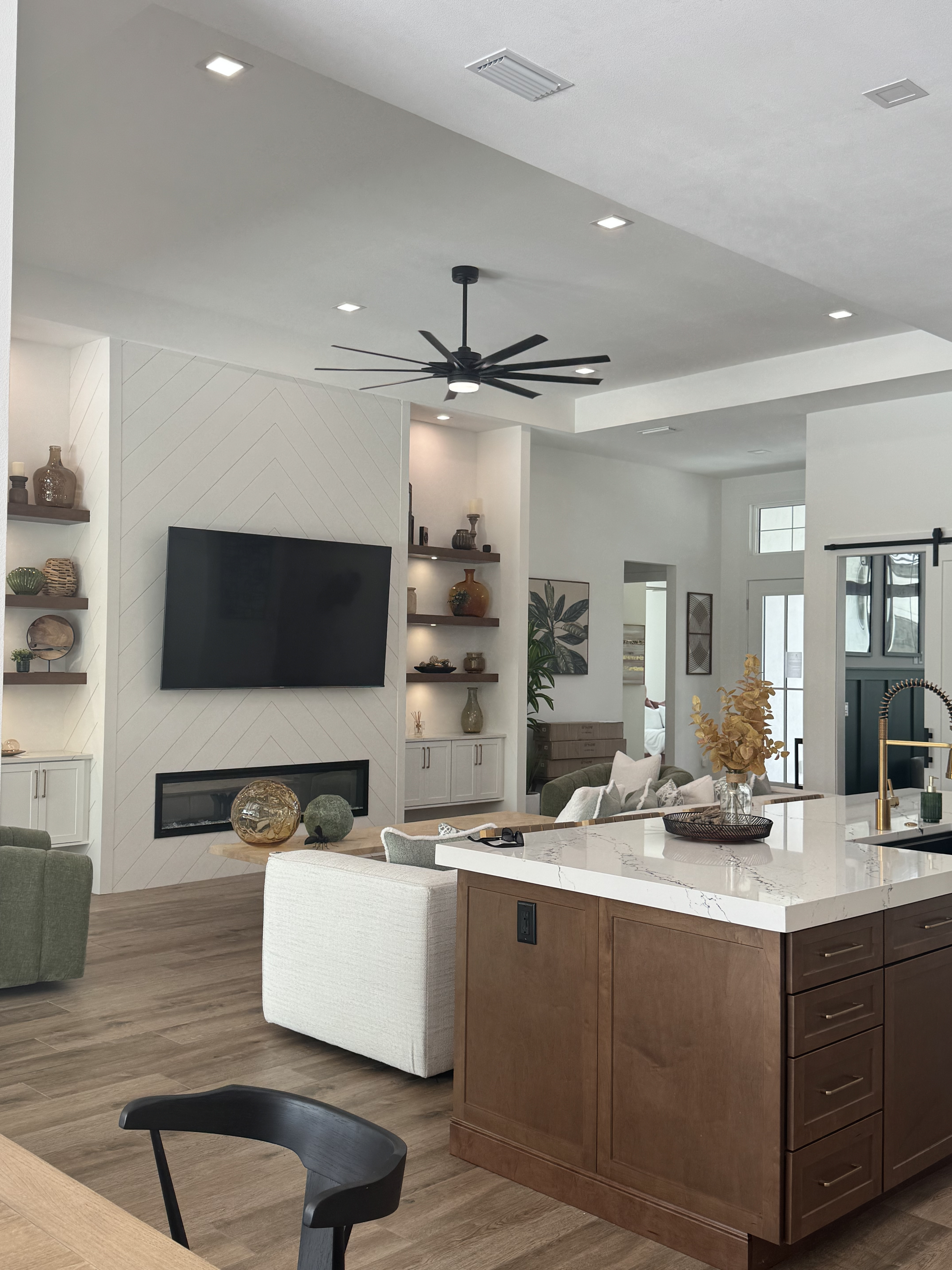  angled view of a living room from behind a kitchen island with marble countertops and a tv hanging on the wall