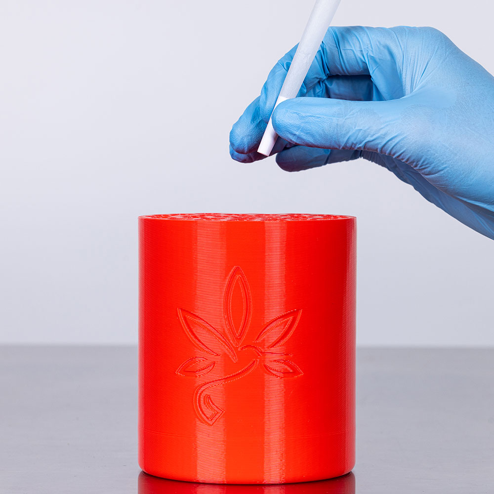 a lit pre rolled refined white rolling paper cone being held in a hand with a red background