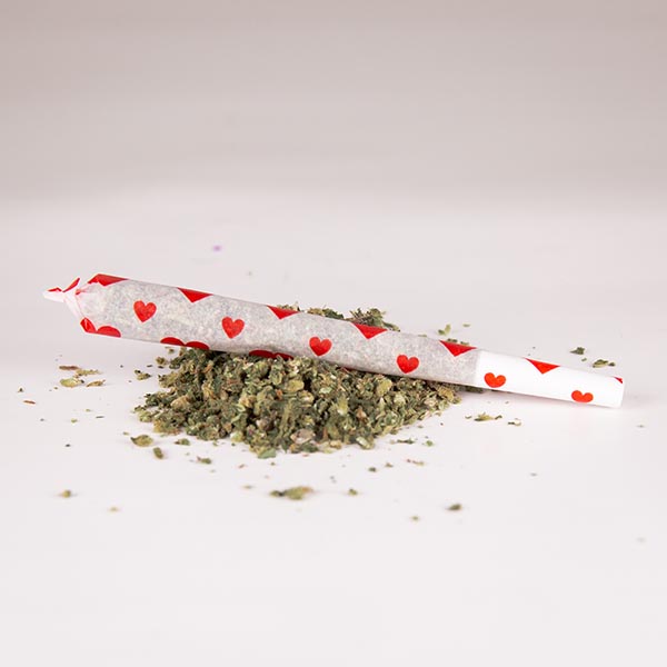 A filled heart printed pre-rolled cone on a pile of cannabis