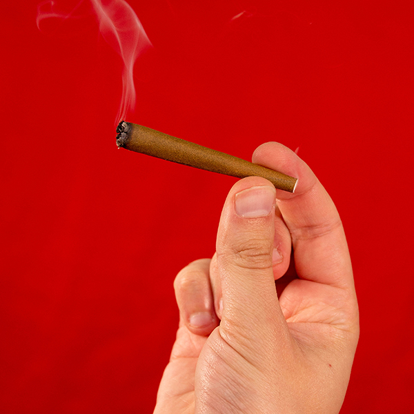 a smoking pre rolled refined white rolling paper cone being held against a red background