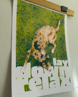 art print displayed in a bamboo clip frame along the top on a white wall. Art print features a dog on a green grass background with white text saying "lay down relax" along the bottom 1/3rd.